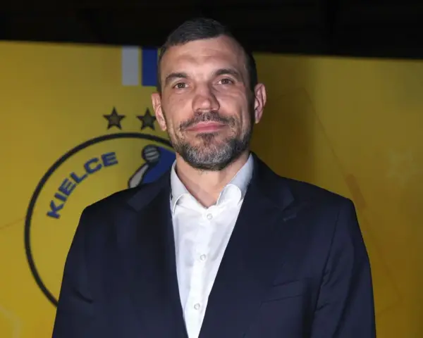 Michał Jurecki w garniturze na tle żółtej ściany z logo "Kielce".