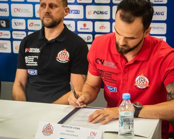 Krzysztof Łyżwa, zawodnik ARGED KPR Ostrovia, podpisuje dokumenty. Obok siedzi trener.