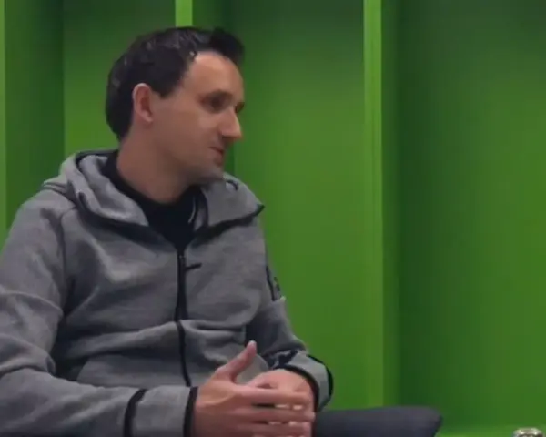 Artur Sadowski w szarej bluzie z kapturem siedzi na tle zielonych ścian, opowiadając o swoich pasjach.