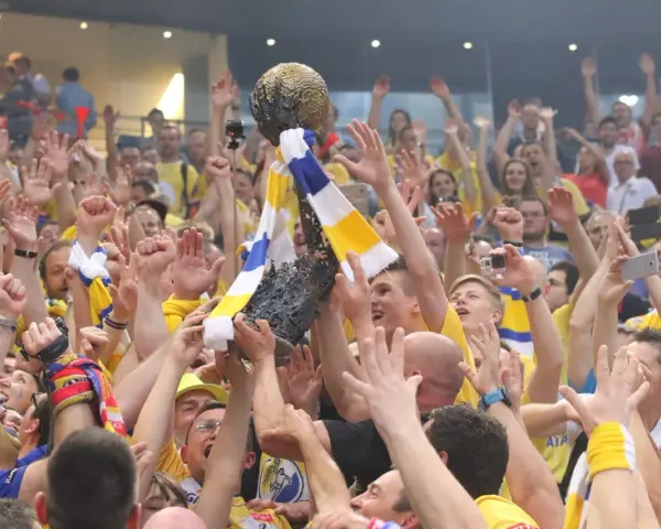 Tłum świętuje zwycięstwo, unosząc puchar. Kibice w żółto-niebieskich barwach, jak na meczach kielce liga mistrzów, cieszą się z sukcesu.