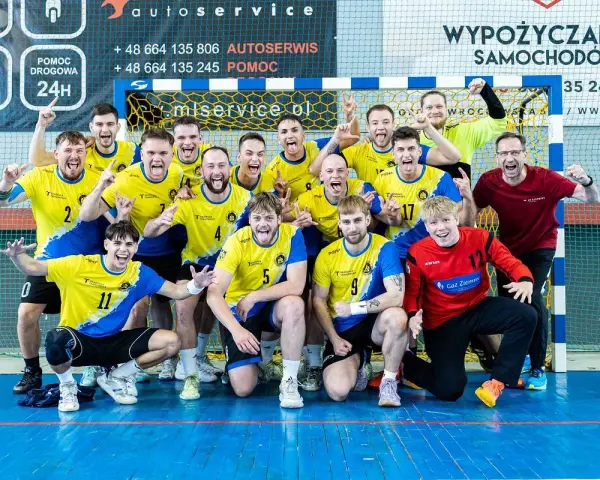 Drużyna Unii Tarnów piłka ręczna świętuje zwycięstwo. Radośni zawodnicy w żółto-niebieskich strojach pozują do wspólnego zdjęcia.