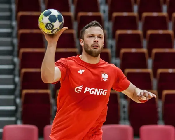 Mateusz Przybylski w czerwonej koszulce z orłem i logo PGNiG, gotowy do rzutu piłką ręczną.
