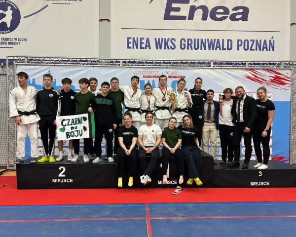 Młodzi sportowcy świętują sukces na mistrzostwa polski juniorów. Drużyna z transparentem "Czarni do boju" pozuje na podium.