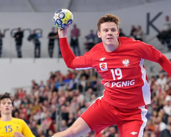 Jan Czuwara w akcji, rzuca piłką do bramki. Zawodnik w czerwonej koszulce z numerem 19.