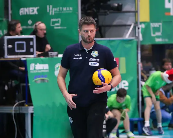 Trener Michał Piwowarczyk z piłką siatkową w dłoni, gotowy do akcji na boisku.