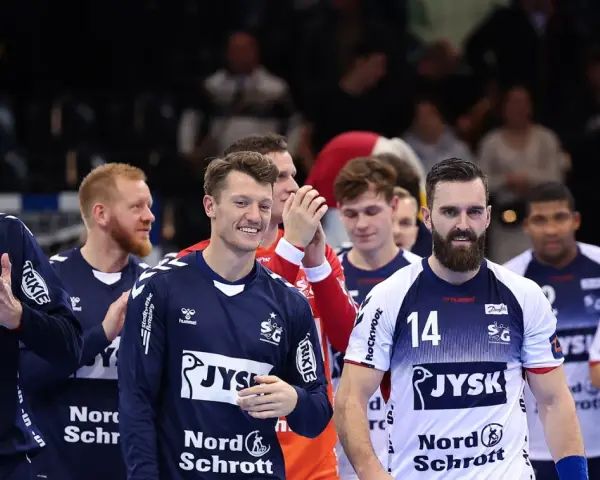Emil Jakobsen z brodą i numerem 14 na koszulce, w otoczeniu drużyny piłkarzy ręcznych.