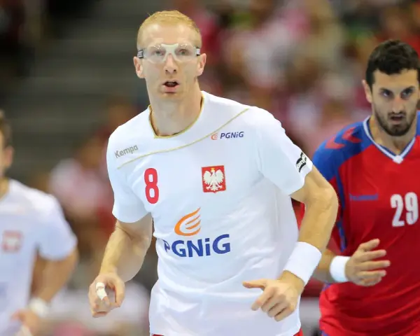 Kamil Bielecki w okularach ochronnych, z numerem 8 na koszulce, biegnie podczas meczu. Obok zawodnik z numerem 29.