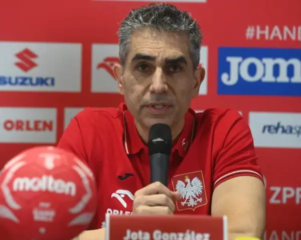 Jota González, trener reprezentacji Polski w piłce ręcznej, przemawia do mikrofonu. Obok niego czerwona piłka.