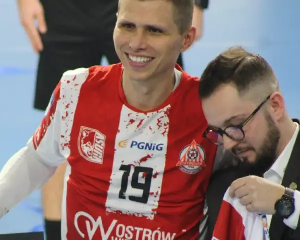 Uśmiechnięty Bartłomiej Tomczak w czerwonej koszulce z numerem 19, obok niego mężczyzna w garniturze.