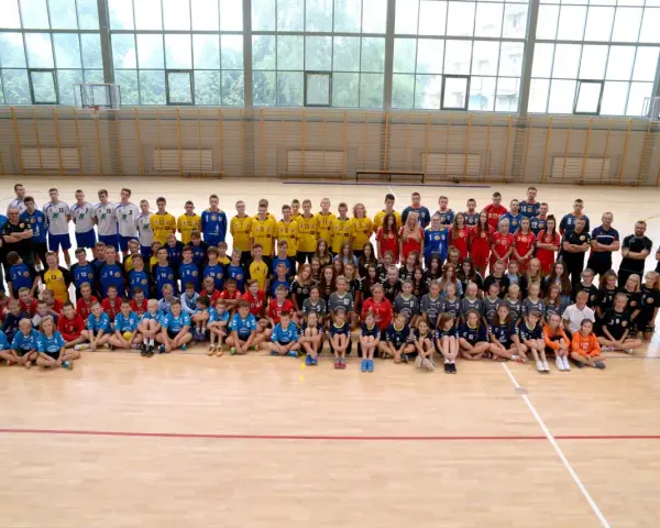 Drużyna Olimp Grodków na hali sportowej. Duża grupa dzieci i młodzieży w strojach sportowych pozuje do wspólnego zdjęcia.