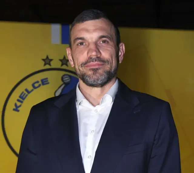 Michał Jurecki w garniturze na tle żółtej ściany z logo "Kielce".