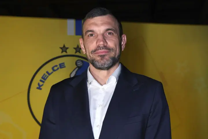 Michał Jurecki w garniturze na tle żółtej ściany z logo "Kielce".