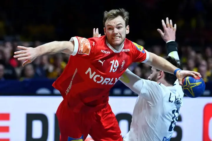 Mathias Gidsel w czerwonej koszulce z numerem 19, w akcji podczas meczu piłki ręcznej, walczy o piłkę.
