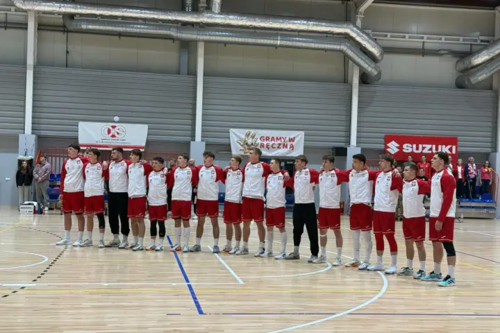 Drużyna w strojach biało-czerwonych, w tym Filip Jankowski, stoi na parkiecie hali sportowej.