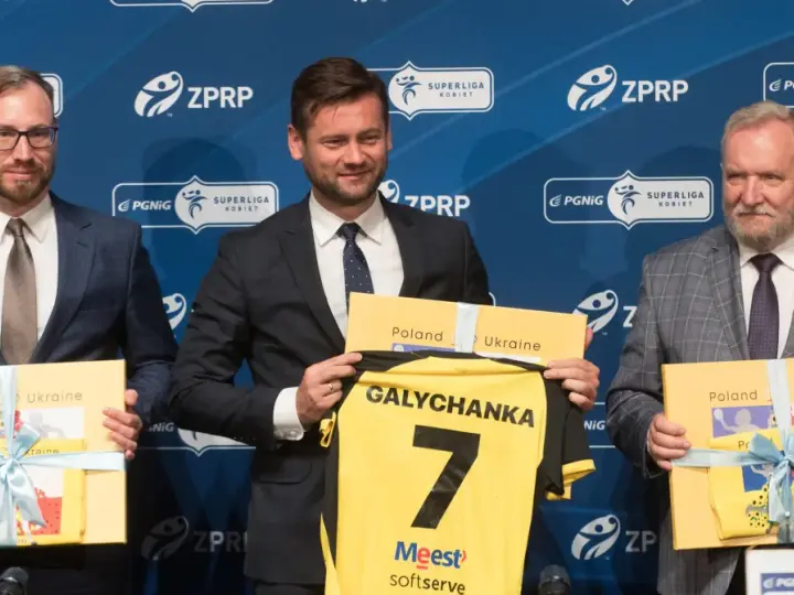 Trzech mężczyzn w garniturach prezentuje koszulkę z napisem "Galychanka" i numerem 7. Obok nich żółte pudełka z napisami "Poland Ukraine".