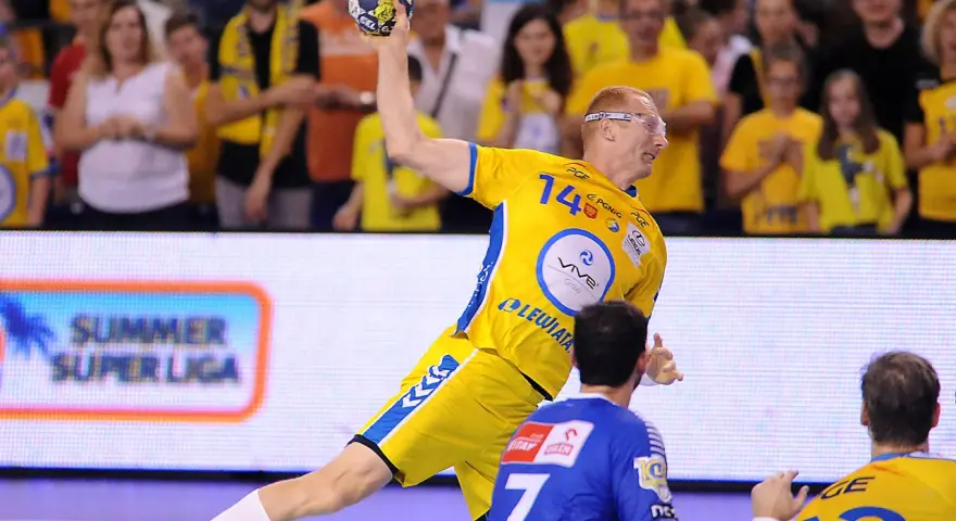 Piłkarz ręczny w żółtej koszulce z numerem 14 rzuca piłkę podczas eliminacji mistrzostw europy w piłce ręcznej grupa polska.