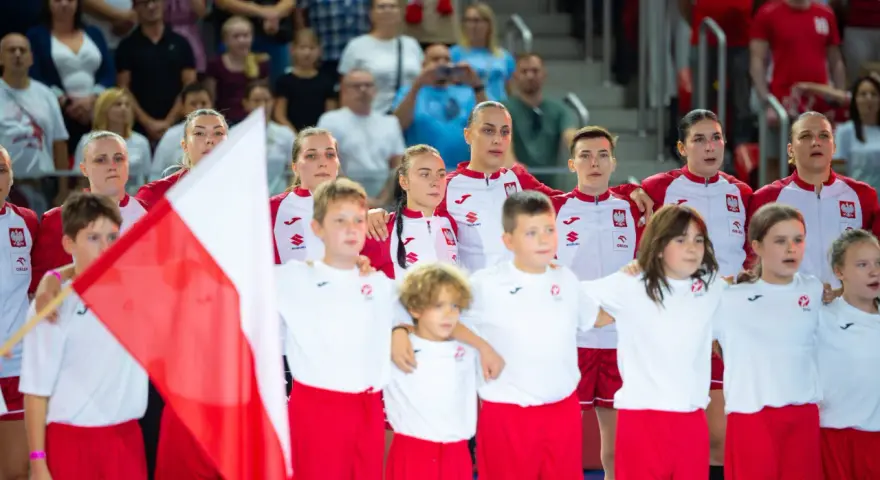 Młode zawodniczki i zawodnicy w strojach reprezentacji Polski, z biało-czerwoną flagą, przed meczem piłka ręczna kobiet mistrzostwa świata.