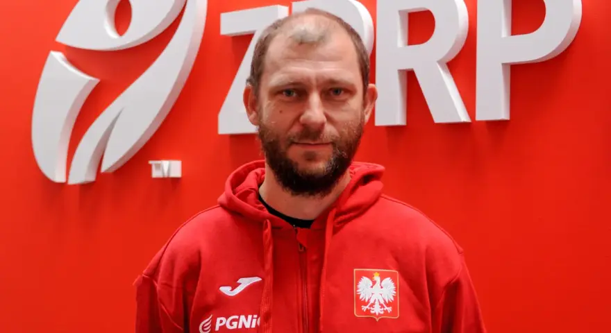 Marcin Wichary, w czerwonej bluzie z orłem, przed logo ZRP.