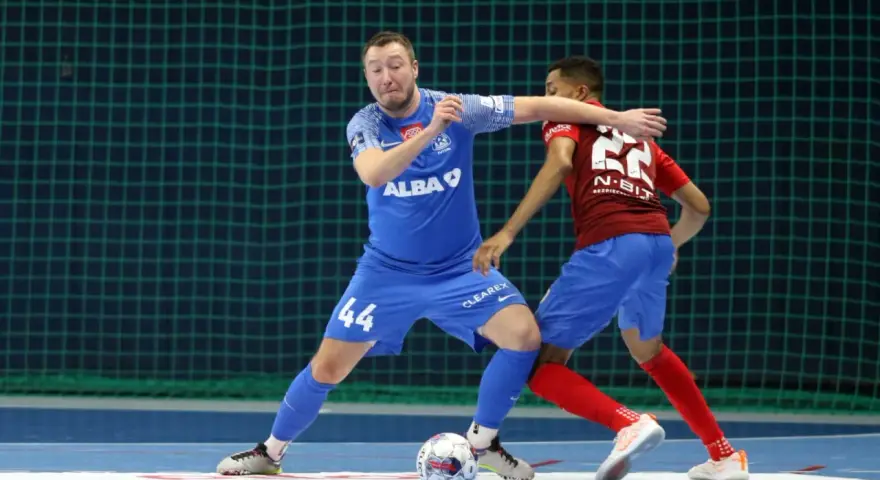 Jakub Grzybowski w akcji, walczy o piłkę z przeciwnikiem na boisku futsalowym.