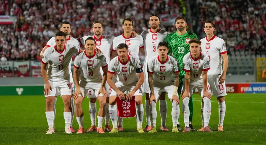 Reprezentacja Polski zawodnicy w białych strojach, gotowi do gry. Na murawie widać dumę i determinację.