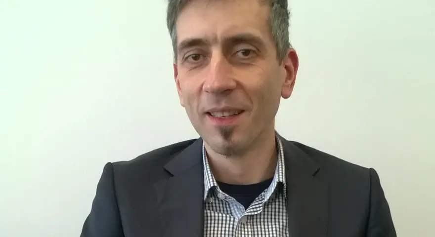 Maciej Kasprzak w czarnym garniturze i koszuli w kratę, z charakterystyczną bródką.