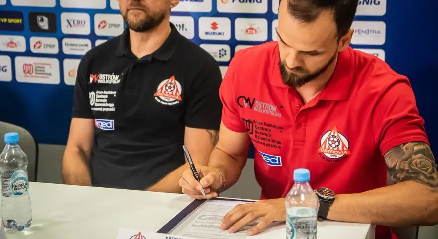 Krzysztof Łyżwa, zawodnik ARGED KPR Ostrovia, podpisuje dokumenty. Obok siedzi trener.