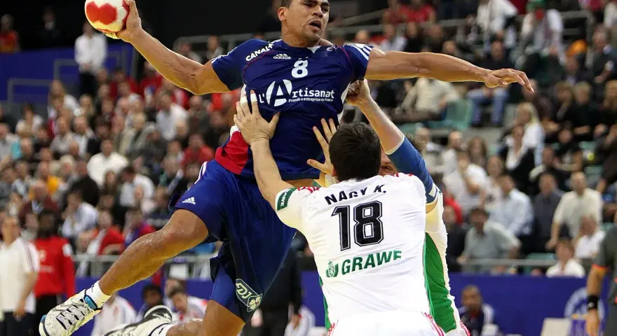 Daniel Narcisse w skoku rzuca piłką do bramki, otoczony przez obrońców.