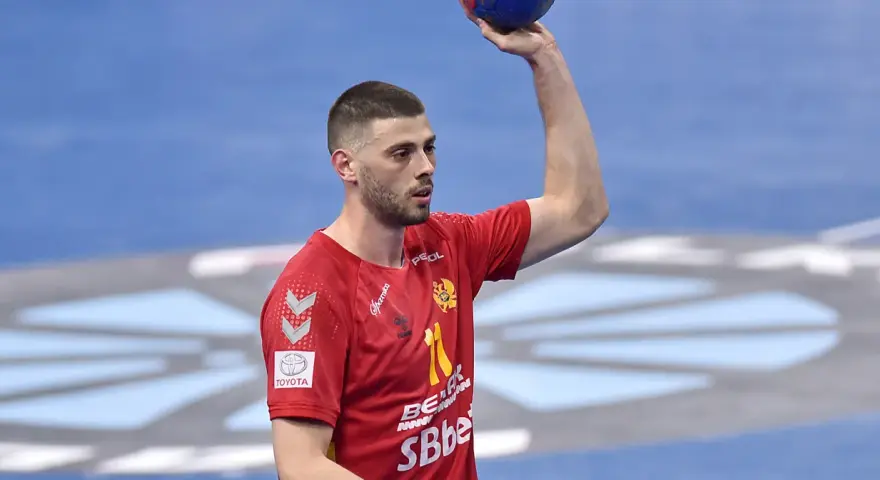 Branko Vujović, zawodnik piłki ręcznej, w czerwonej koszulce z numerem 11, trzyma piłkę nad głową.