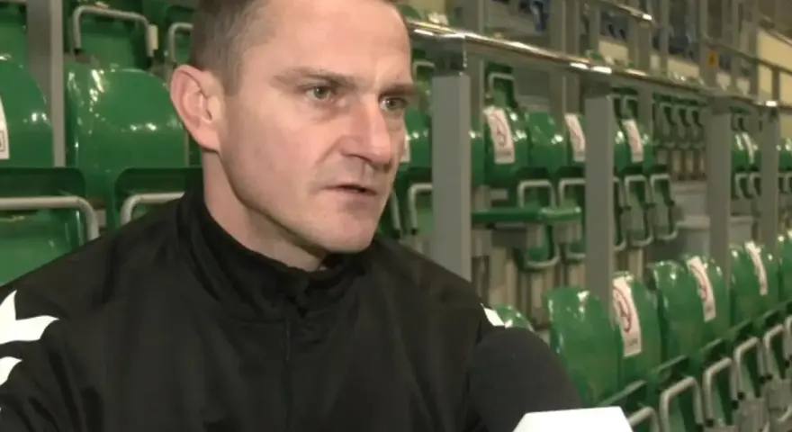 Marcin Pilch udziela wywiadu przed rzędem zielonych krzesełek na trybunach.