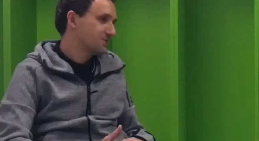 Artur Sadowski w szarej bluzie z kapturem siedzi na tle zielonych ścian, opowiadając o swoich pasjach.