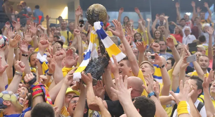 Tłum świętuje zwycięstwo, unosząc puchar. Kibice w żółto-niebieskich barwach, jak na meczach kielce liga mistrzów, cieszą się z sukcesu.