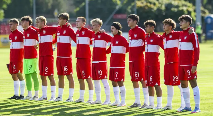 Drużyna Polski na Mistrzostwach Europy do lat 17. Piłkarze w czerwonych strojach z białymi pasami stoją w rzędzie, gotowi do meczu.