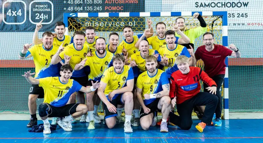 Drużyna Unii Tarnów piłka ręczna świętuje zwycięstwo. Radośni zawodnicy w żółto-niebieskich strojach pozują do wspólnego zdjęcia.