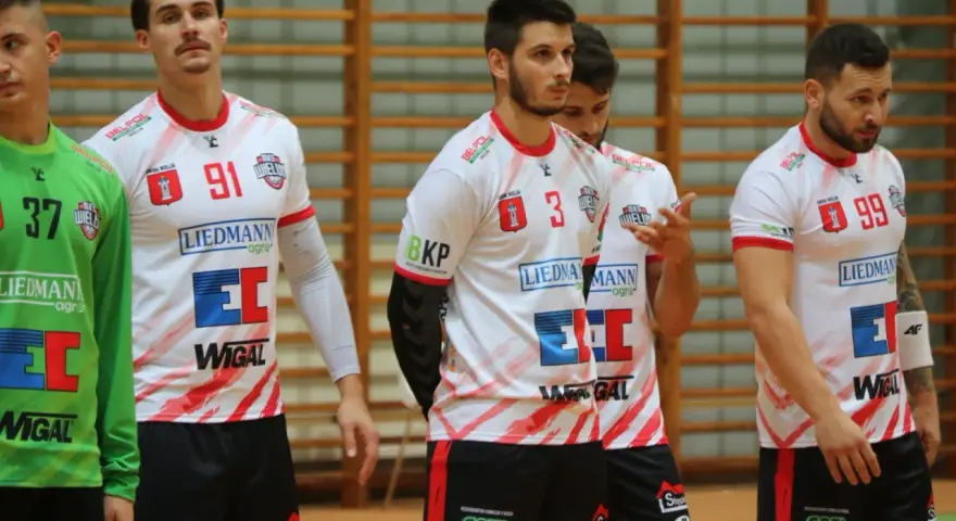 Szymon Kucharski i koledzy z drużyny w białych strojach z czerwonymi detalami, gotowi do gry.