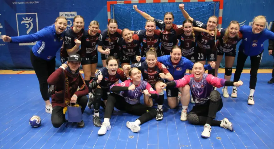Drużyna piłki ręcznej KPR Bukowsko Dopiewo świętuje zwycięstwo. Radosne zawodniczki w strojach sportowych, z numerami na koszulkach, pozują do zdjęcia z trenerem.