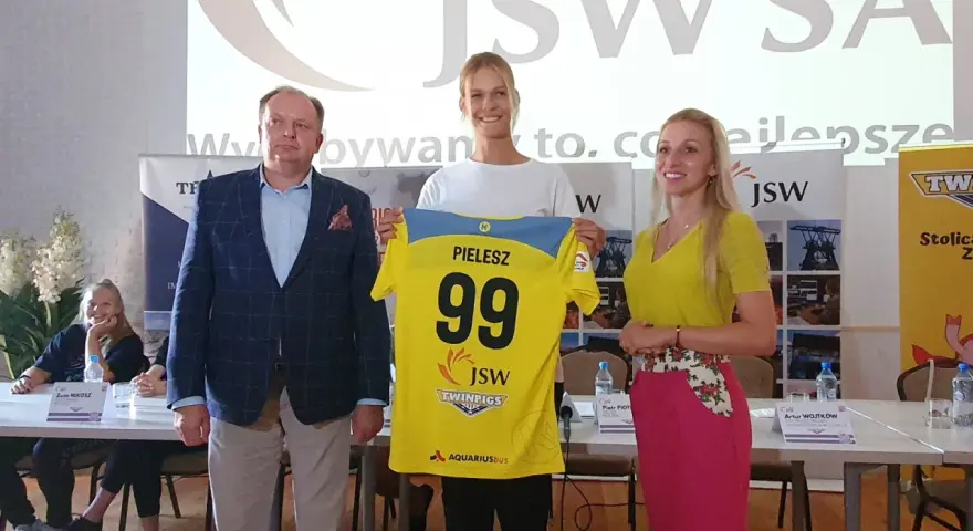 Trzy osoby pozują z koszulką z numerem 99 i nazwiskiem PIELESZ. W tle logo JSW i napisy związane z firmą, być może z okazji wydarzenia w MTS Żory.