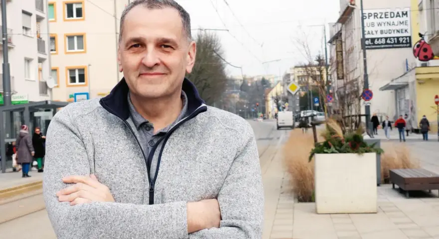Sebastian Pieńkowski stoi na tle miejskiej ulicy z tramwajami i budynkami.
