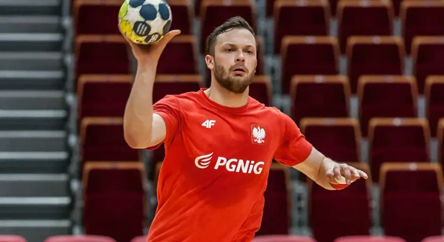 Mateusz Przybylski w czerwonej koszulce z orłem i logo PGNiG, gotowy do rzutu piłką ręczną.