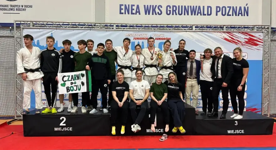 Młodzi sportowcy świętują sukces na mistrzostwa polski juniorów. Drużyna z transparentem "Czarni do boju" pozuje na podium.