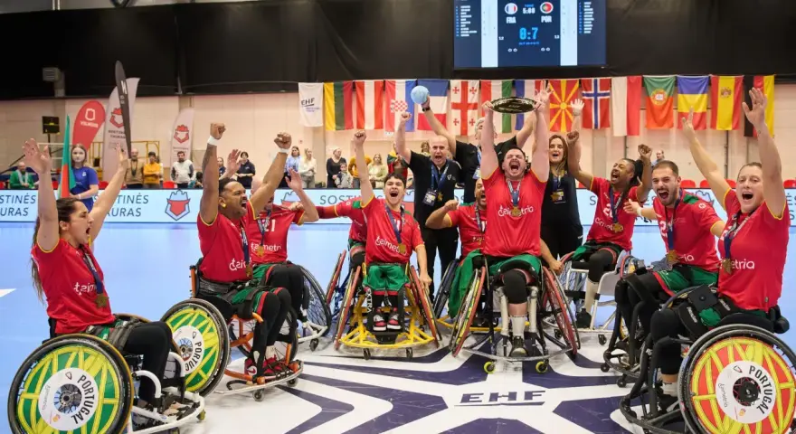 Drużyna Portugalii w piłce ręcznej na wózkach świętuje zwycięstwo. Na ekranie wynik meczu, a w tle flagi państwowe i logo EHF.