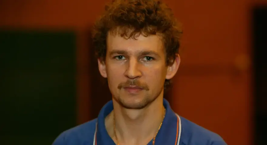 Tomasz Wronka, z kręconymi włosami i wąsami, w niebieskiej koszulce polo.