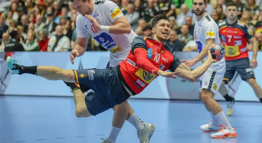 Piłkarz ręczny Hiszpanii w czerwonej koszulce z numerem 10 wykonuje rzut. W tle inny zawodnik i kibice.
