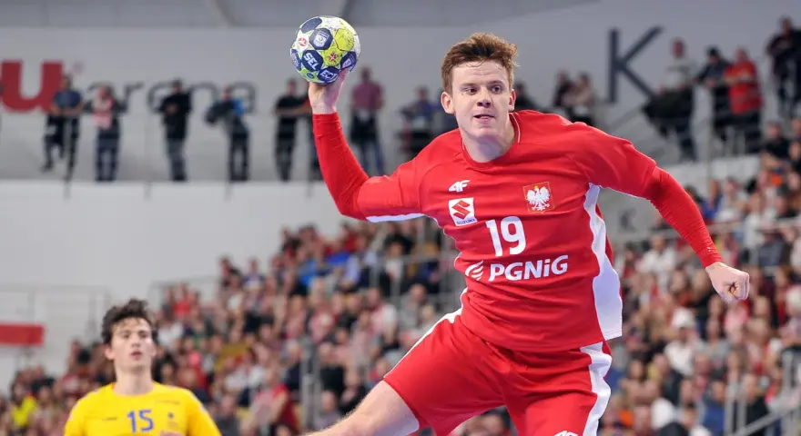 Jan Czuwara w akcji, rzuca piłką do bramki. Zawodnik w czerwonej koszulce z numerem 19.