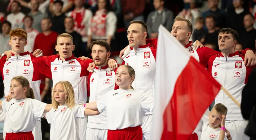 Polska drużyna piłki ręcznej z flagą narodową. Młodzi zawodnicy i dzieci w strojach biało-czerwonych.