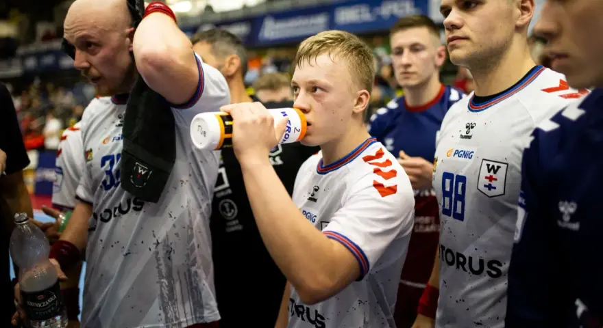 Szymon Adamczyk pije wodę z bidonu, otoczony kolegami z drużyny.