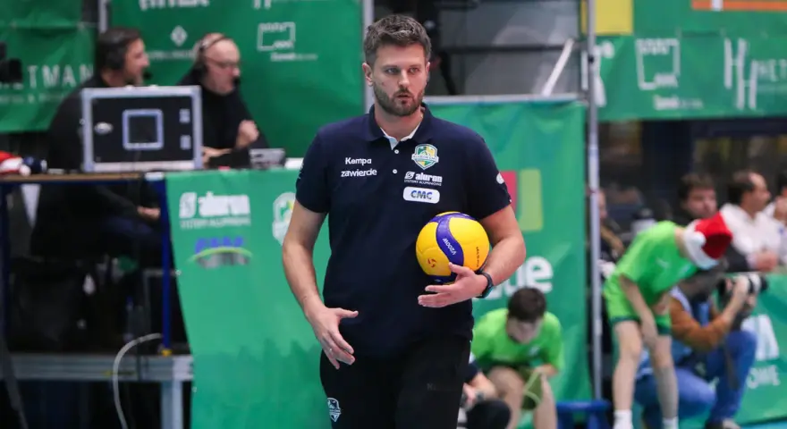 Trener Michał Piwowarczyk z piłką siatkową w dłoni, gotowy do akcji na boisku.