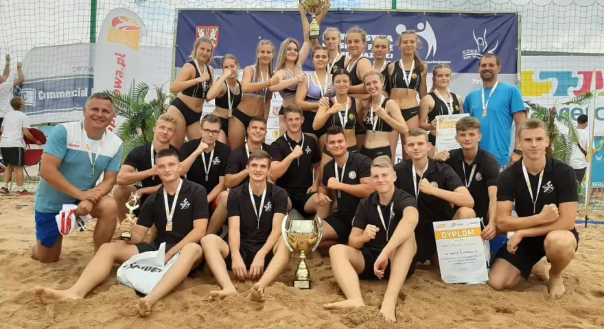 Drużyna MKS Mazur Sierpc świętuje zwycięstwo na piasku, trzymając puchary i dyplomy.