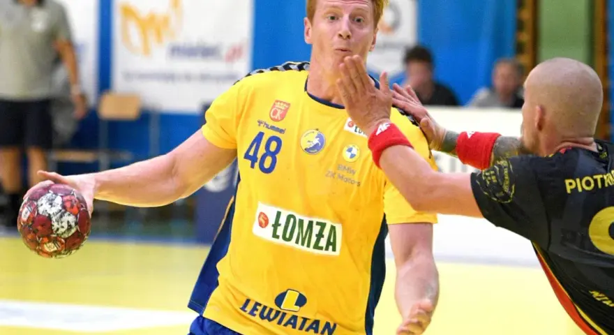 Tomasz Gębala w żółtej koszulce z numerem 48 łapie piłkę do ręcznej, broniąc się przed przeciwnikiem.
