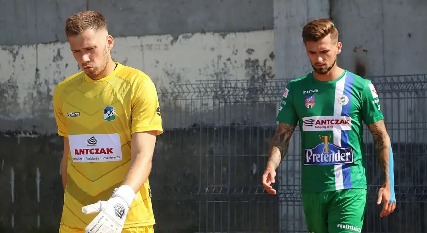 Dwóch piłkarzy, w tym Michał Kaszuba w żółtej koszulce bramkarza, idzie obok siebie.