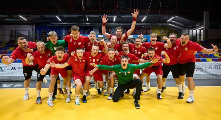 Drużyna piłkarzy ręcznych w czerwonych strojach świętuje zwycięstwo. Wśród nich Krzysztof Zimny, bramkarz w zielonym stroju, klęczy z wyciągniętymi rękami.